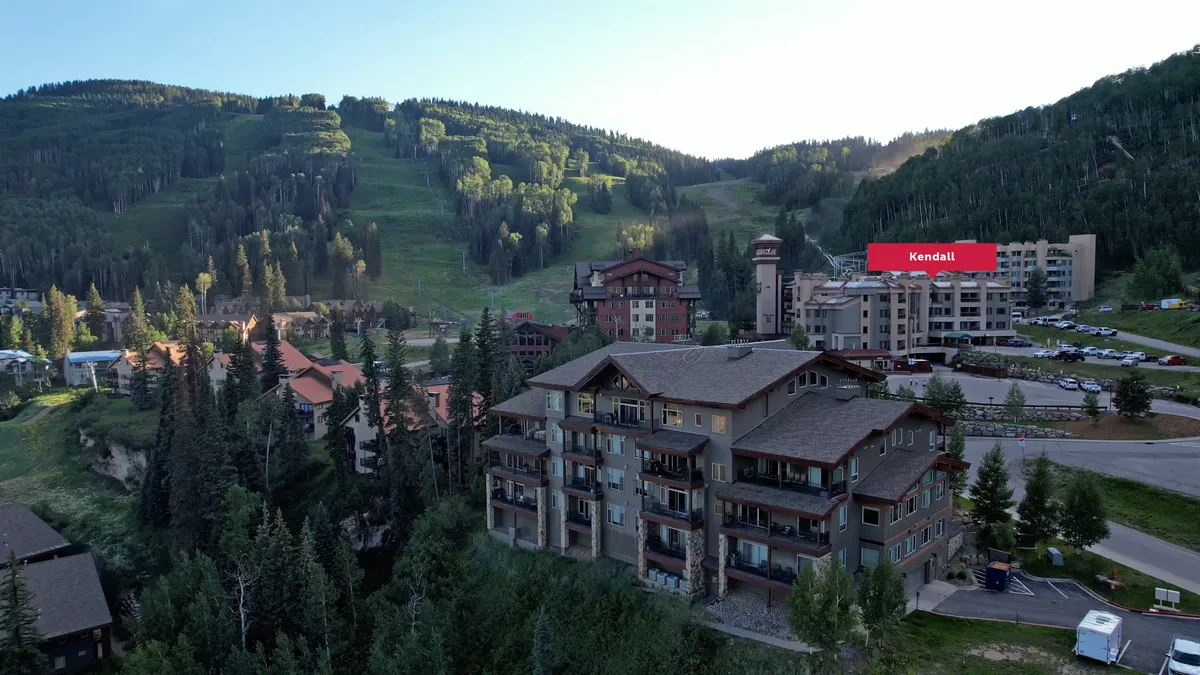 A picturesque exterior view of the resort buildings surrounded by a tree line and mountain landscape. The scene hints at various amenities, including outdoor gathering spaces and serene spots for relaxation, with a natural backdrop perfect for both adventure and downtime.