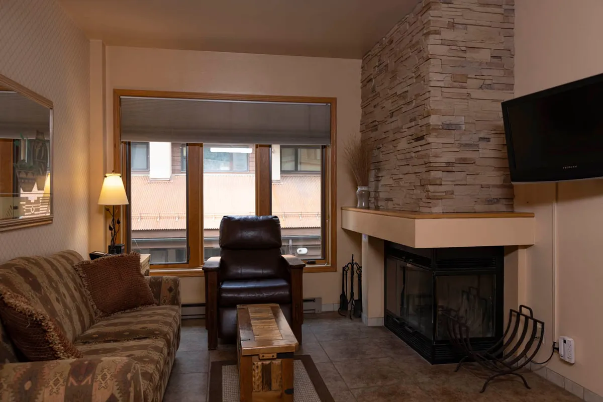 A stylish living area featuring a crackling fireplace, a recliner and sofa, and a view out a window to the snowy outdoors. The setup invites intimate gatherings, reading by the fire, or simply soaking in the warmth after a day in the mountains.