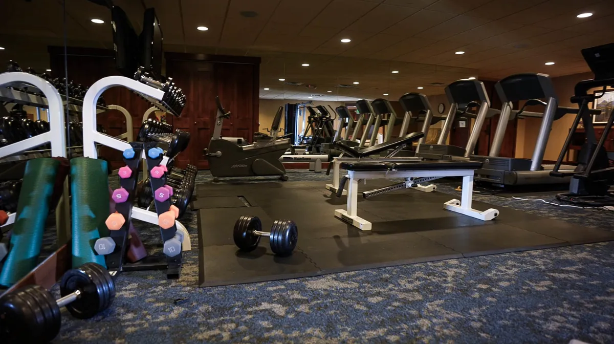 A bright, modern fitness center interior with dumbbells, treadmills, and a weight bench, evoking an uplifting and focused mood. The space appears welcoming and well-equipped for guests seeking to stay active during their visit.